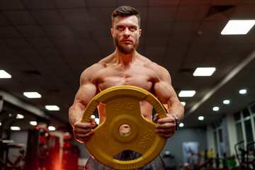 Front view. Man has workout in the gym. Having exercise with pancakes for the rod.