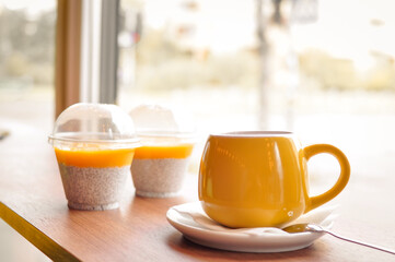 Yellow cup of coffee with dessert on wooden table 