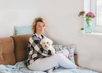 a woman is sitting at home on the couch and stroking her favorite white dog