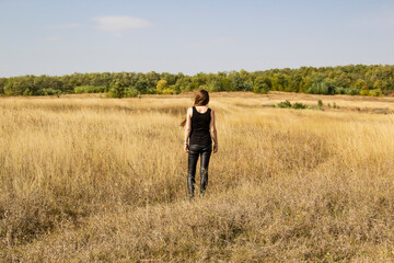 Naklejka na ściany i meble Beautiful young dark haired woman in black clothes stand in field.