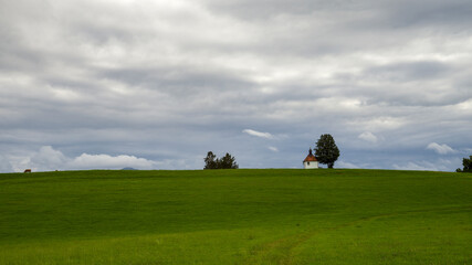 Gr&uuml;ne Wiese mit kleiner Kirche vor bew&ouml;lktem Himmel