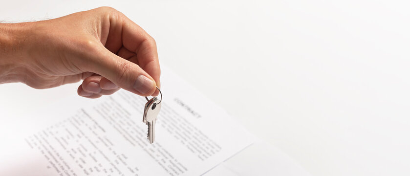 Close-up Of Hand Of Man Holding A Key From A New Apartment Over Table With Contract