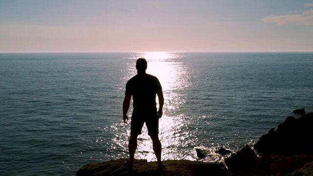 Silueta de hombre en un acantilado frente al reflejo del sol en el mar lavantando los brazos un d&aacute;a sensacional. Desde Conil, C&aacute;diz, Andaluc&iacute;a, Espa&ntilde;a, Europa.