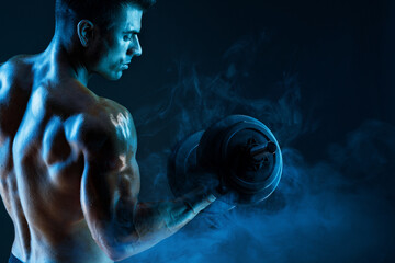 Muscular model sports young man with dumbbells in hand on dark background. Fashion portrait of...