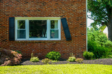 Large window on the brick front wall of a house with a black shutter that is broken and falling off