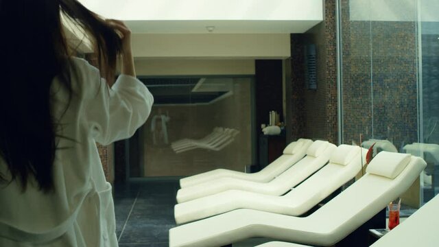 Sexy woman taking off bathrobe in spa center. Pretty girl relaxing on deckchair.