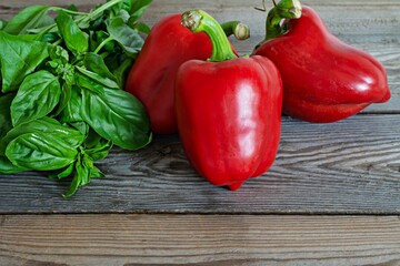 Ripe red bell pepper (paprika) with fresh green basil on wooden background, healthy food concept, vegan food.