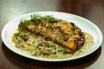 Homemade potato pancake on a white plate with mushroom sauce, whole pieces of mushrooms sprinkled with herbs. Potato pancakes with mushroom cream, sprinkled with herbs.