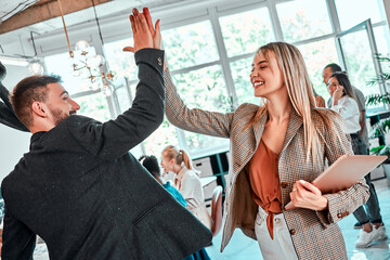 Beautiful business woman is giving high five and smiling to man in office