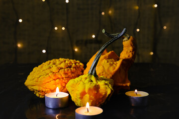 various decorative pumpkins and burning candles on background of blurry garland lights, dark mysterious atmosphere and home decoration for a scary Halloween night