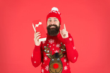 happy bearded man wearing funny knitted sweater and santa claus hat and hold present box has an idea for celebrating new year party, new year shopping