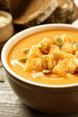 Tasty creamy pumpkin soup with croutons and seeds in bowl on wooden table, closeup
