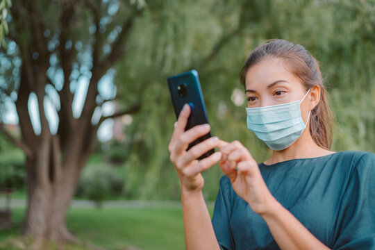 Woman wearing face mask using mobile phone for contact tracing app while walking outside during coronavirus pandemic. People city lifestyle.
