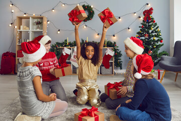 Group of happy multiethnic children exchanging presents sitting on floor in living-room