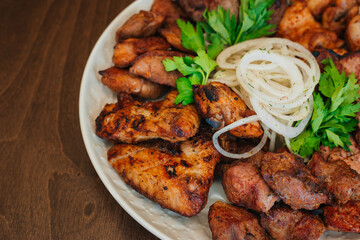 Fried meat on a white plate with onions and herbs. Appetizing barbecue. Chunks of beef on a platter. On a dark wooden background