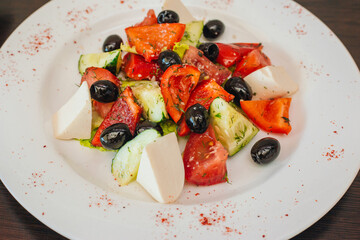 Diet salad of olives, cheese and tomatoes with cucumbers on a white plate. Healthy eating. Dish on a dark wooden background