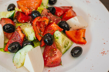 Diet salad of olives, cheese and tomatoes with cucumbers on a white plate. Healthy eating. Dish on a dark wooden background