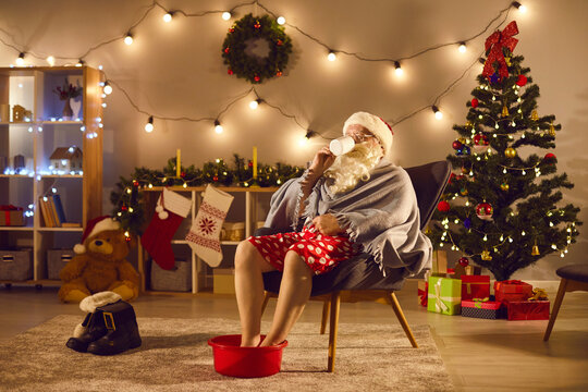 Santa Relaxing At Home After Long Day Of Work, Enjoying Cup Of Tea And Soaking Feet In Warm Water