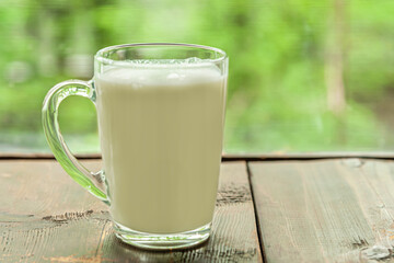 fresh organic milk in a glass mug on a wooden table near the window