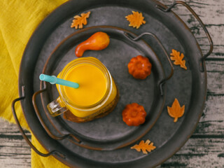 
pumpkin soup and pumpkin.
Pumpkin soup in a mug with a straw, small pumpkins and decor leaves lie on iron plates, close-up top view.