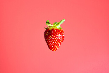 One red strawberry soaring in the air. Food levitation concept. Pink background.