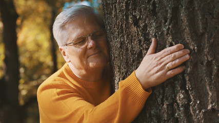 An older man lovingly hugging and leaning face to tree trunk feels relaxed and good on the autumn day. High quality photo