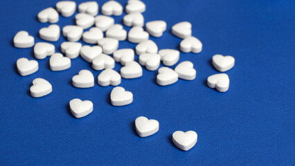 Pills in the shape of a heart poured out from the bottle on the blue surface of the table at the pharmacy. Isolated background. Blue background.