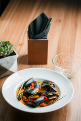 Gourmet serving of spicy tomato soup with fried mussels and chili peppers on a plate and wooden table isolated. Delicious seafood mussels . Lemon and baguette . Clams in the shells. Top view.