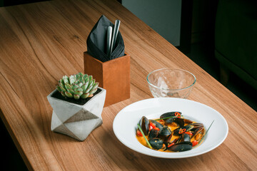 Gourmet serving of spicy tomato soup with fried mussels and chili peppers on a plate and wooden table isolated. Delicious seafood mussels . Lemon and baguette . Clams in the shells. Top view.