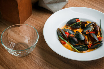 Gourmet serving of spicy tomato soup with fried mussels and chili peppers on a plate and wooden table isolated. Delicious seafood mussels . Lemon and baguette . Clams in the shells. Top view.