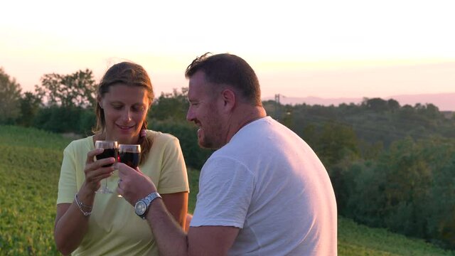 young couple takes an aperitif drinking a glass of red wine at sunset exchanging cuddles
