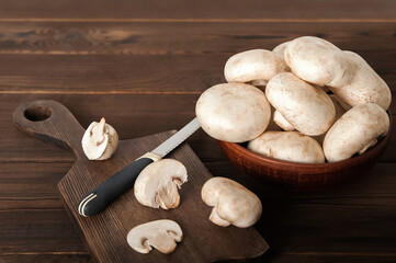 Mushrooms in a plate on a dark wooden board. Champignons and knife close up and copy space.