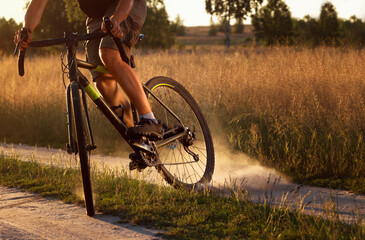 Cyclist in a field at sunset. Young sporty guy on a bicycle raise up dust from the rear wheel after a skid. Close-up. © Chinart