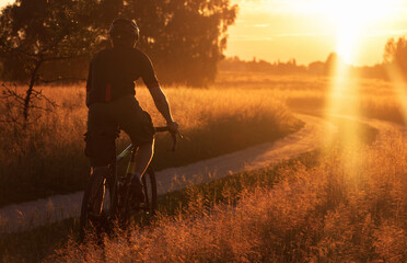 Cyclist riding a trail in a field on a gravel bike on a dramatic sunset background. Sport and...