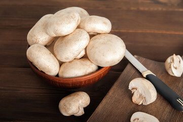 Mushrooms in a plate on a dark wooden board. Champignons and knife close up and copy space.