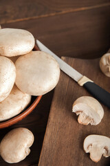 Mushrooms in a plate on a dark wooden board. Champignons and knife close up and copy space.