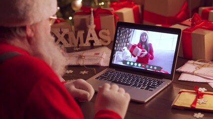 Over shoulder view of Santa Claus video calling kid girl on laptop talking to child by webcam open Christmas gift box in virtual online chat meeting using computer sit at home table greeting on xmas.