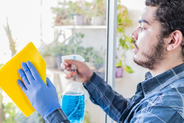 Young man sprayer and cloth cleaning window glass. Casual young man with a beard.