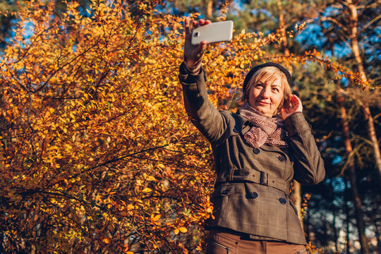 Middle-aged woman taking selfie on smartphone. Senior lady having fun in autumn forest