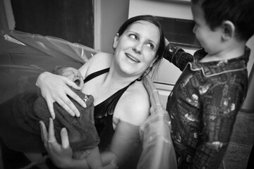 Little Boy Comforting Mother Holding Newborn Baby in Birthing Pool After Home Birth