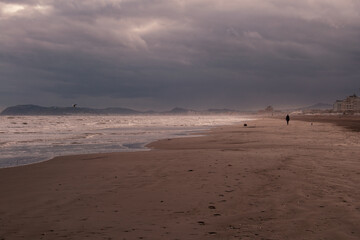 person walking alone on the beach on a cloudy and cold day