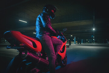 Motorbiker is standing at night street in the neon lights.