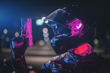 A cyberpunk biker concept. Motorbiker in a helmet with a toy gun is standing on a night city street...