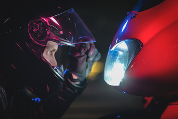 A motorbiker with open helmet visor is looking on his motorbike close up.