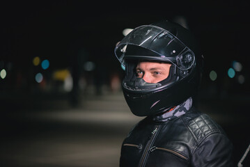 Motorbiker in a helmet with open visor is standing on a night city street.