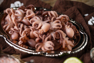 Close-up view of dish with baby octopuses on rustic wooden table with brown napkin background. Delicious meal. Concept of oh healthy tasty food from the ocean or sea.