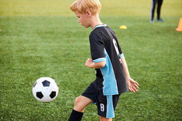 young kid boy training with soccer ball alone in stadium, practice various tricks, before game