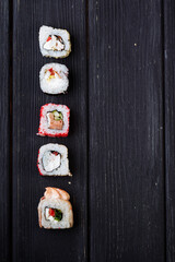 Japanese sushi rolls lying on a black wooden board. View from above.