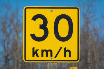 A yellow speed warning sign showing a speed limit of 30 km/h