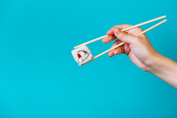Woman's hand holds Tasty sushi roll maki with wooden chopsticks on blue background close up. Place for caption and text © lightscience